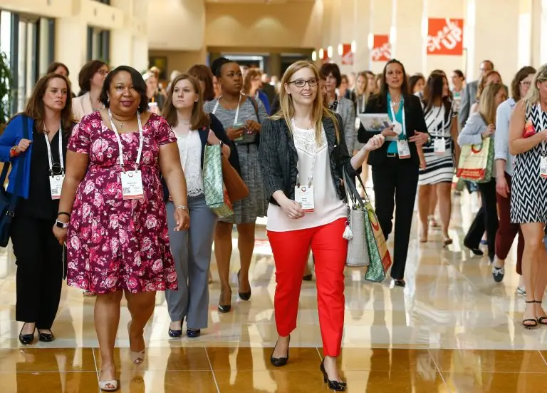Conference attendees wearing badges walking together through a bright lobby.