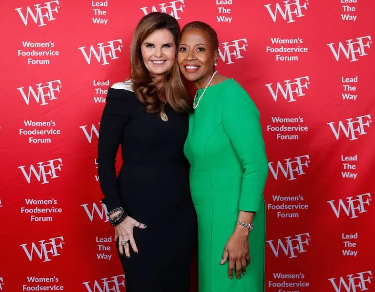 Two women posing together in front of a red Women's Foodservice Forum backdrop.