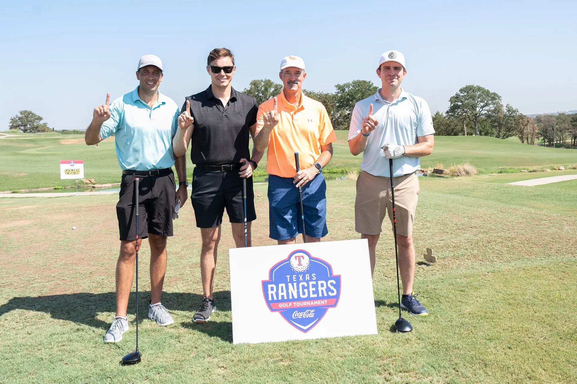 Four people posing on a golf course behind a Rangers Foundation sign.