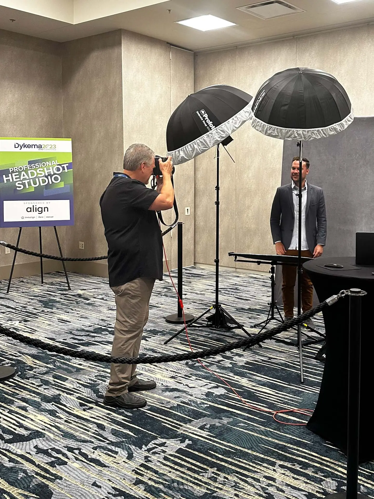 Photographer photographing a suited man between two umbrella lights beside a Dykema headshot studio sign.