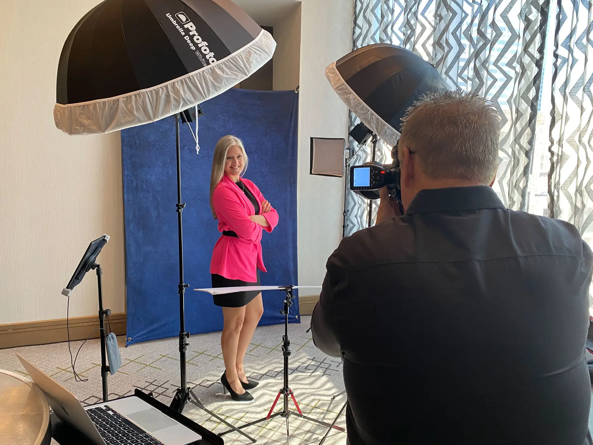 Photographer taking a portrait of a woman in a pink jacket between two studio lights.