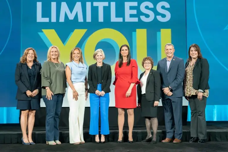 Eight people posing onstage in front of a blue and yellow Limitless You backdrop.