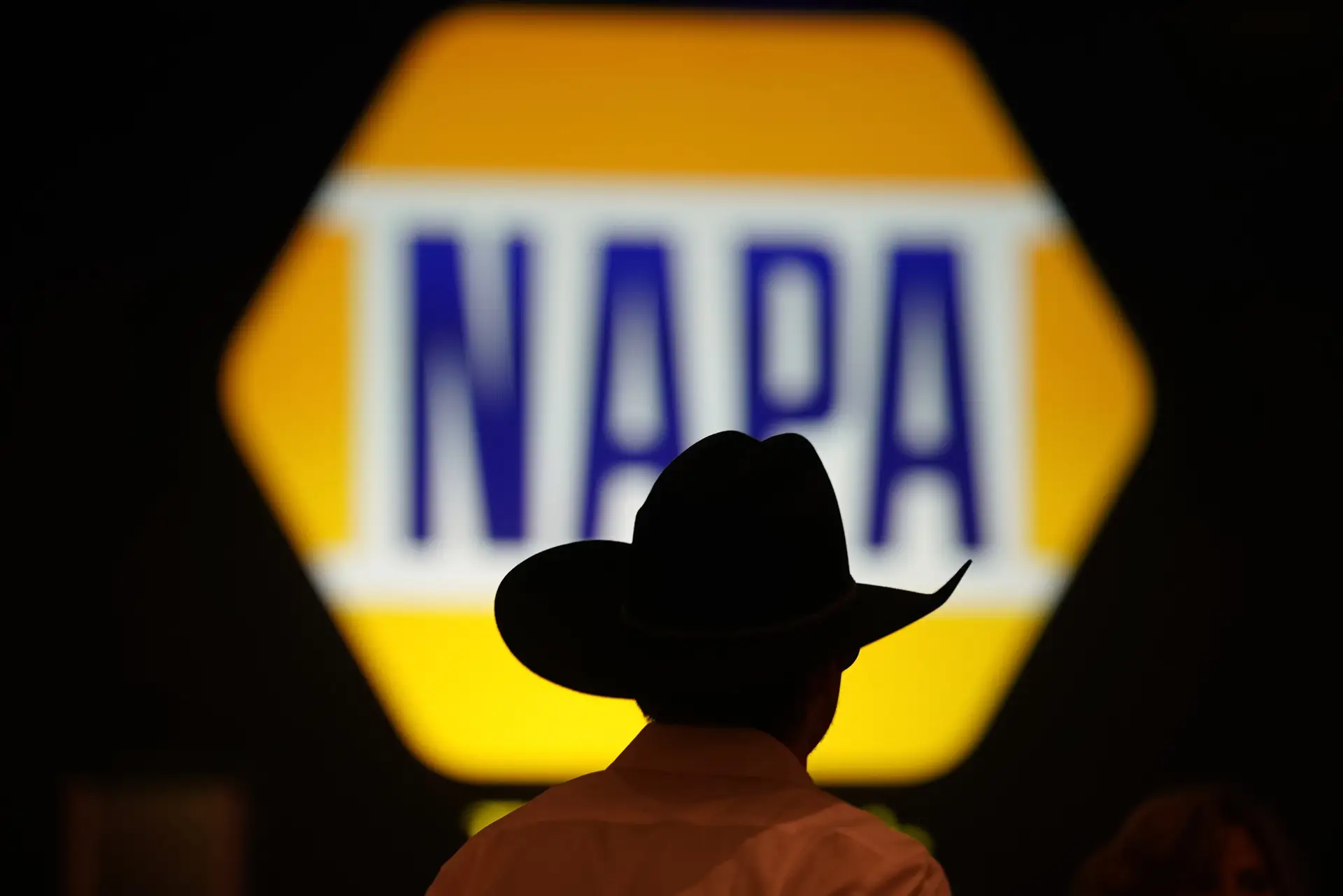 Silhouette of a person in a cowboy hat in front of an illuminated NAPA logo.