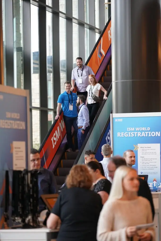 Attendees descending an escalator near an ISM World registration sign.