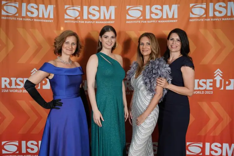 Four women in formal dresses posing in front of an orange ISM backdrop.