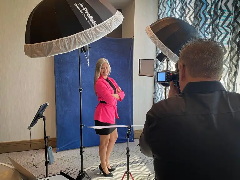 Woman in a pink blazer posing with arms crossed for a corporate headshot against a blue mottled backdrop