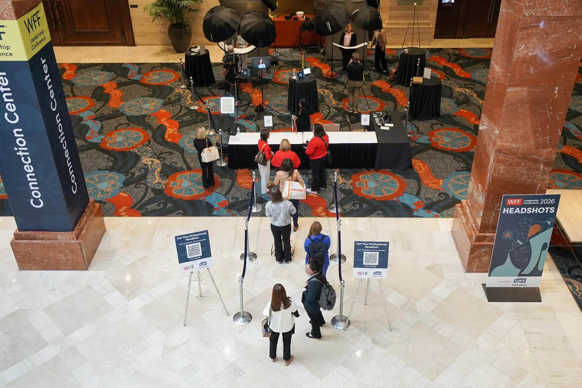 Elevated view of attendees queuing at a headshot check-in table, with WFF Leadership Conference signage and photography setup behind