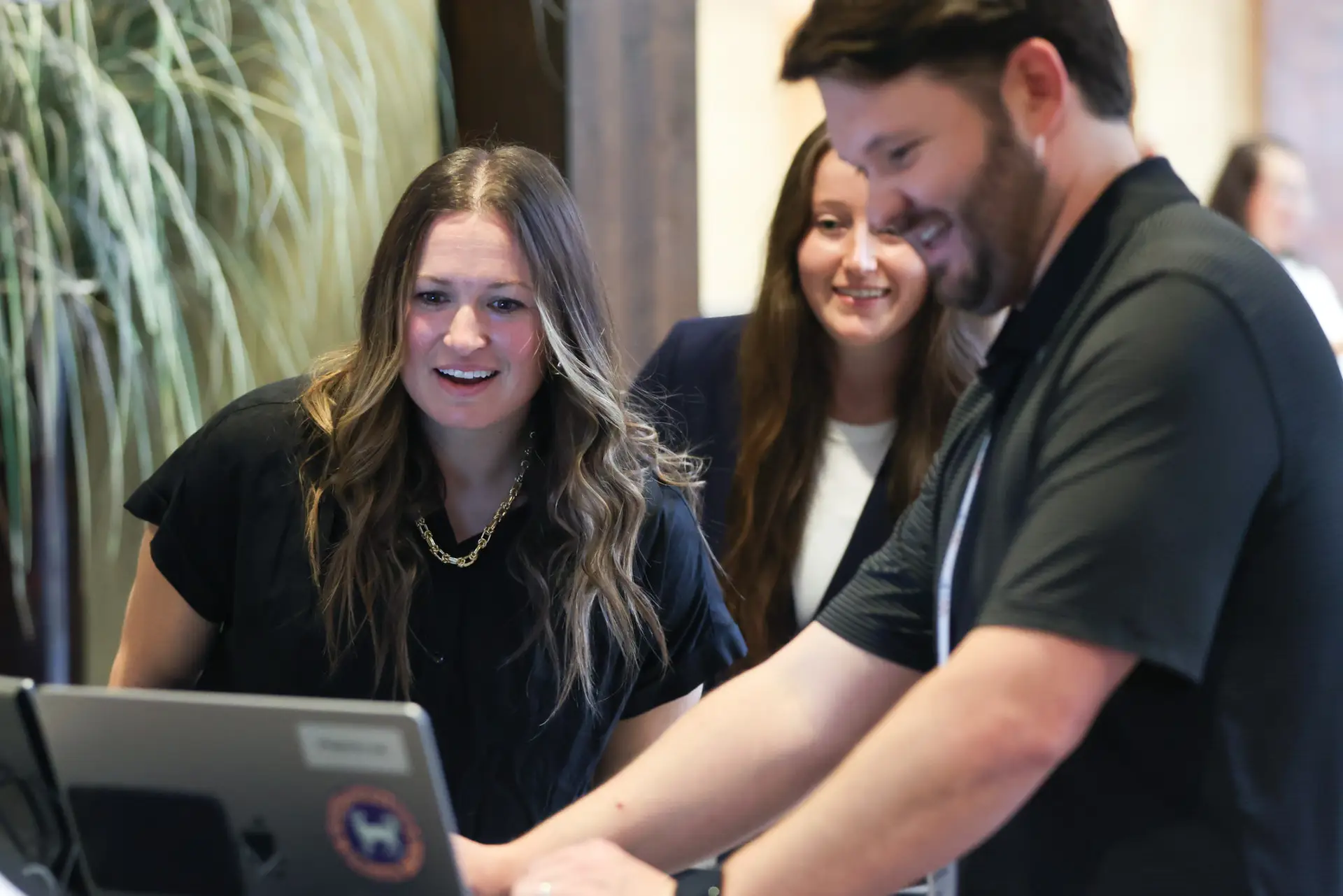 Three conference attendees smiling while looking at a laptop screen together at a headshot review station