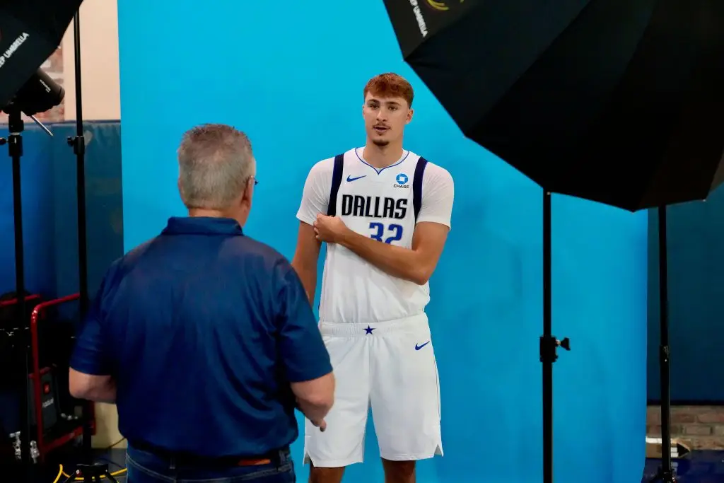 Photographer speaking with a Dallas player in a white number 32 jersey in front of a blue backdrop between professional studio lights